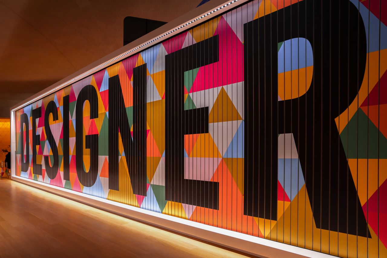 team-02 Vibrant geometric design with 'DESIGNER' text in London gallery.