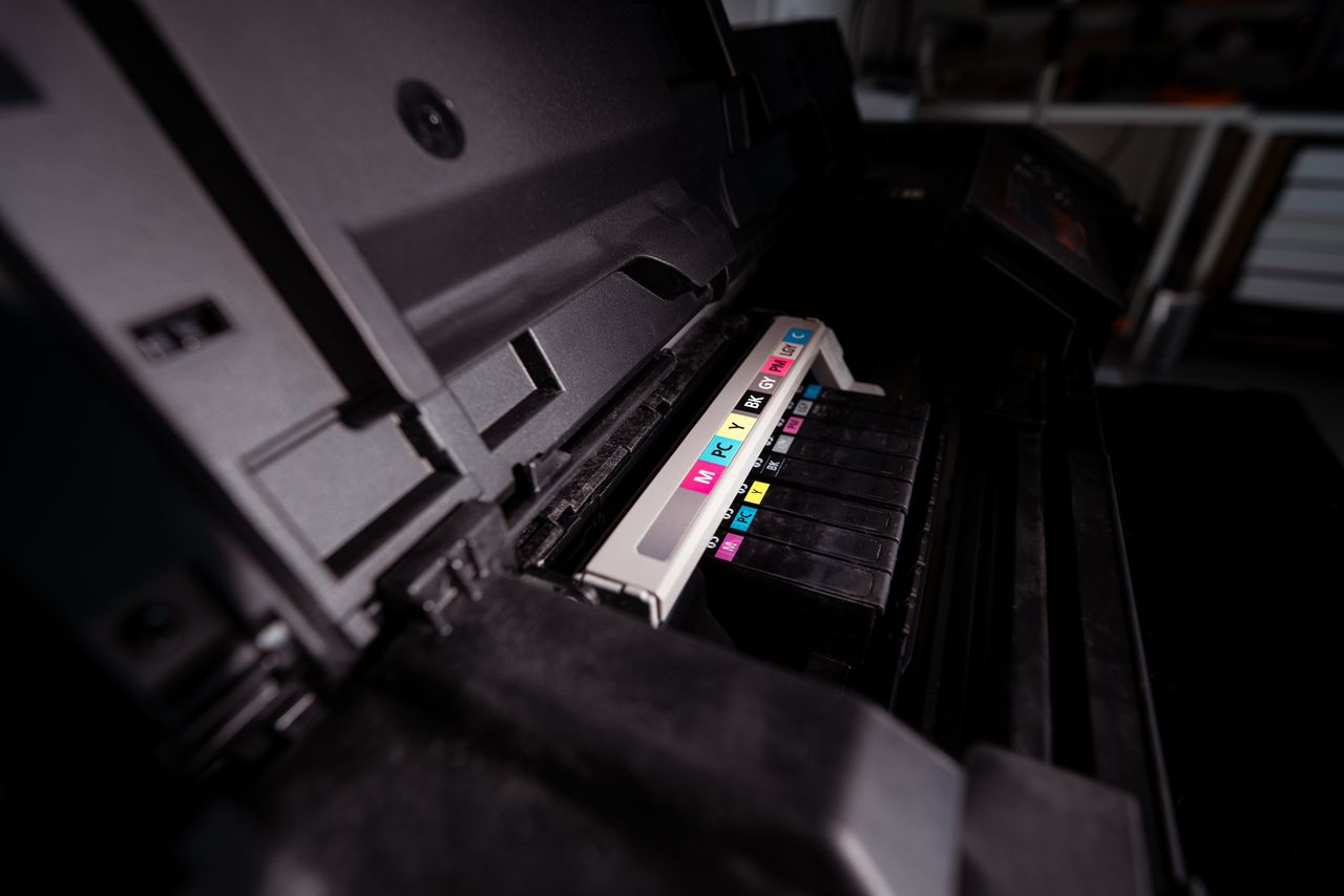 services-01 Detailed view of open printer with visible CMYK ink cartridges in a dark setting.