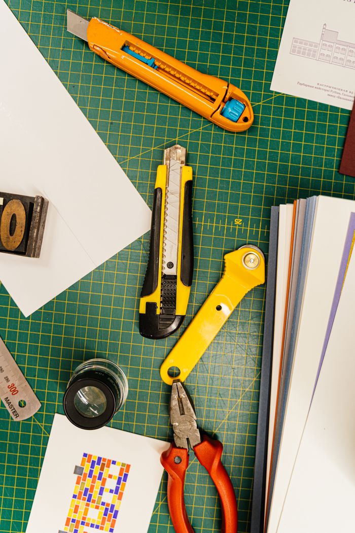 team-04 Top view of various cutting tools on a green grid mat surrounded by papers, ideal for creative projects.